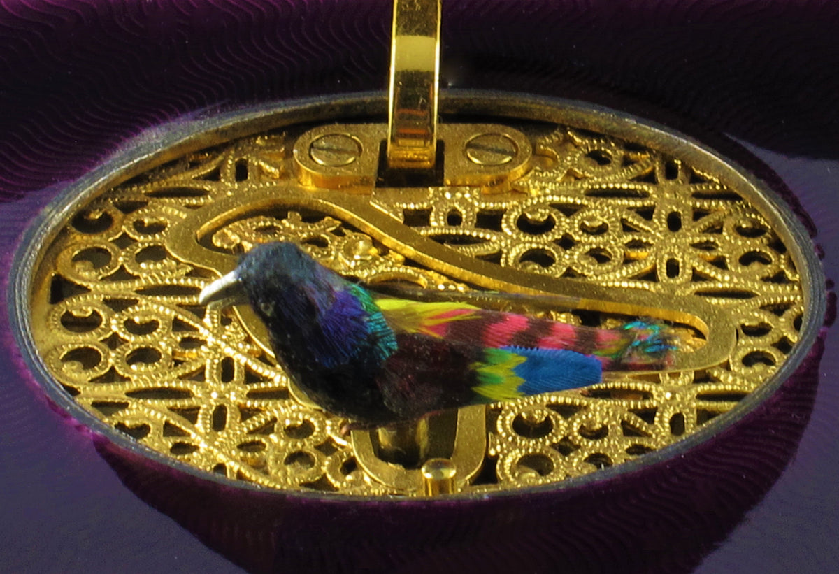 A silver-gilt singing bird automation box with guilloche in translucent violet and green enamel , the oval cover enamelled opening to reveal a singing feathered bird. Swiss 1960